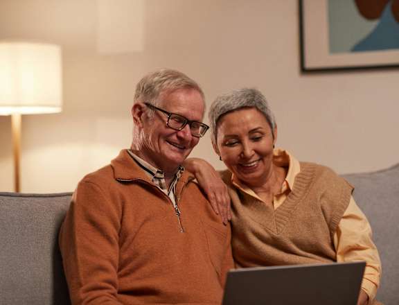 an older couple sitting on a couch using a laptop computer
