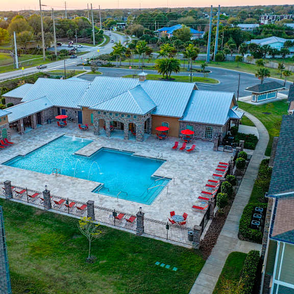 An aerial view of a pool surrounded by red lounge chairs and a building with a blue roof.