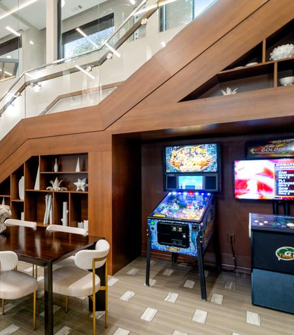 A room with a dining table and chairs, a staircase, and a pinball machine.