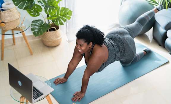 A woman is doing a plank exercise on a blue mat in a well-lit room.