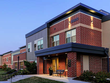 The image shows a modern building with a brick facade and a glass entrance.