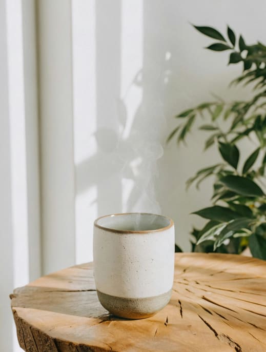 A ceramic cup sits on a wooden stump in front of a plant.