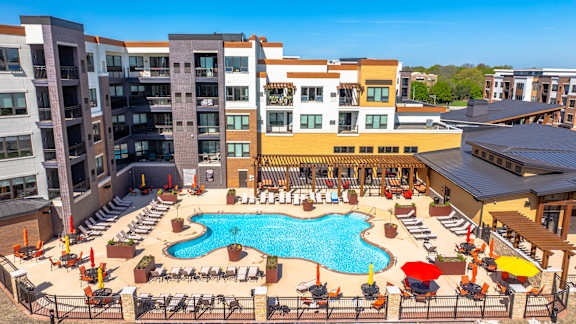 A large pool surrounded by chairs and umbrellas in front of apartment buildings.