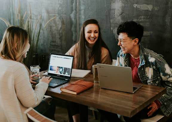 Three people are sitting at a table with laptops open in front of them.