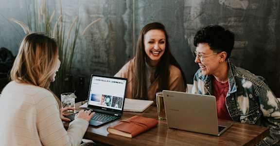 three people sitting at a table with laptops