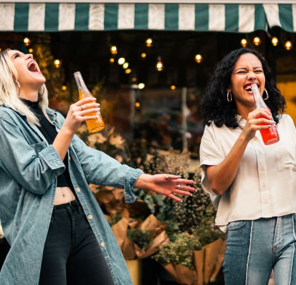 two women drinking beer and laughing while standing outside