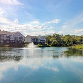 a pond with a fountain in the middle surrounded by apartment buildings