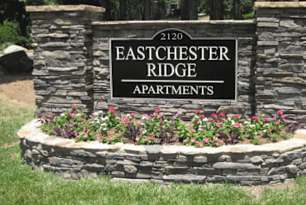 a stone retaining wall with flowers and a sign that says eastchester ridge apartments