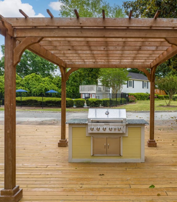a barbecue grill is under a wooden deck with a pergola