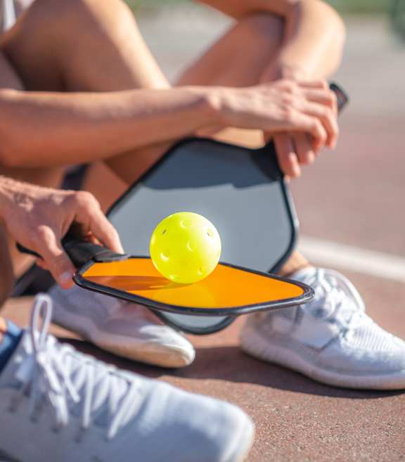 A tennis player is sitting on the ground with a racket and ball in hand.