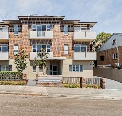 A modern brick apartment building with a front yard and a gate.