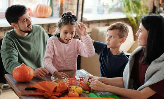 A family is carving pumpkins together at a table.