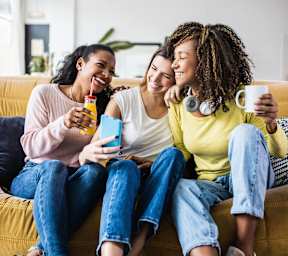 Three people are sitting on a couch, laughing and enjoying drinks.