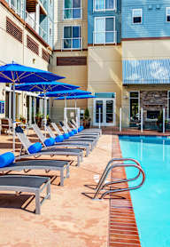A pool with sun loungers and umbrellas in front of a building.