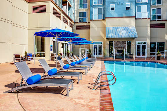 A pool with sun loungers and umbrellas in front of a building.