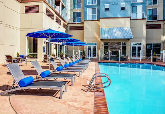 A pool with sun loungers and umbrellas in front of a building.