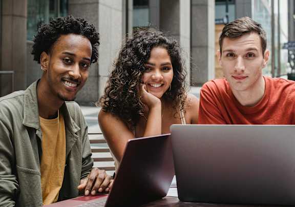 Three people are sitting at a table looking at a laptop.