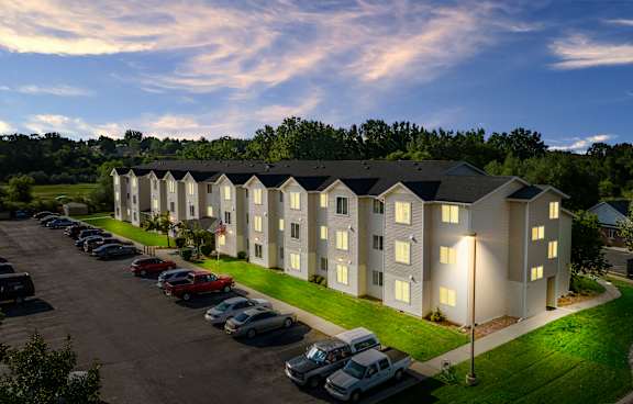 A parking lot with cars and a building with lights on.