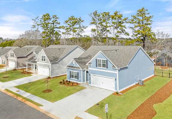 A blue house with a white garage door is in the foreground of a street with other houses in the background.