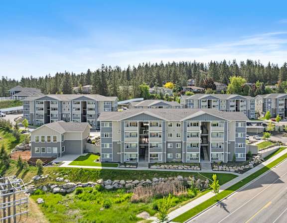A row of modern apartment buildings are surrounded by trees and grassy areas.