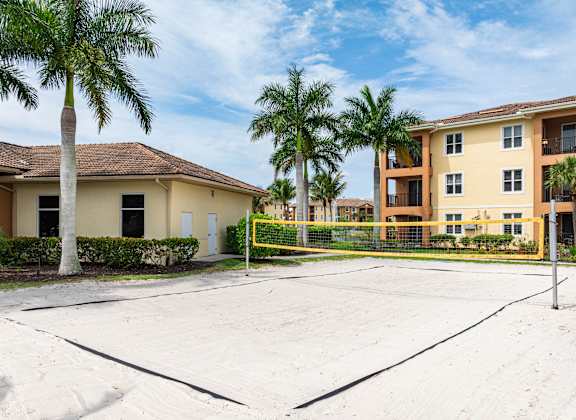 A tennis court is in the foreground of a residential area with apartment buildings and palm trees.