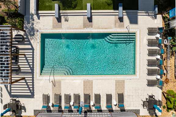 Overhead shot of a rectangular pool with entry steps at both ends and water jets, lined by rows of loungers and a pergola.