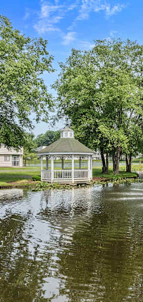 A fountain in the middle of a pond with a gazebo in the background.