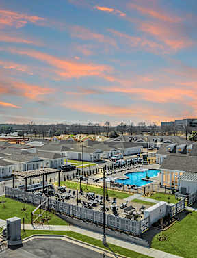 A sunset view of a residential complex with a pool and a large building. at Ovation at Town Madison, Madison