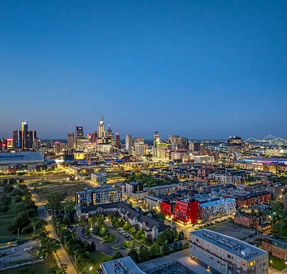 A cityscape at dusk with buildings illuminated and a clear sky.