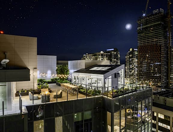 a rendering of the rooftop terrace at night with the city in the background