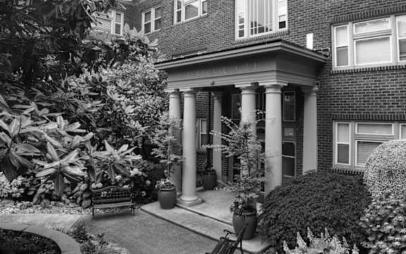 a black and white photo of a house with columns and a bench