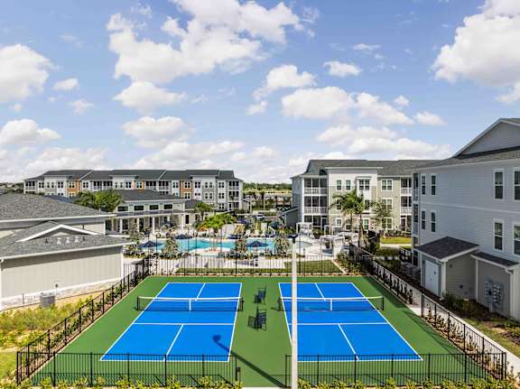 A tennis court is surrounded by a fence and apartment buildings.at Verity Luxury Apartments, Vero Beach, FL 32960
