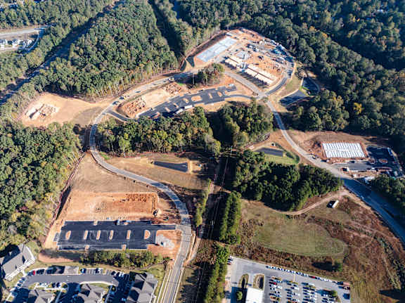 An aerial view of a construction site surrounded by trees and a parking lot.