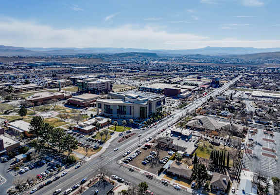 A large building with a blue roof is surrounded by a parking lot and other buildings.