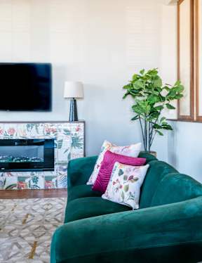 A green velvet sofa with a potted plant and a television in the background.