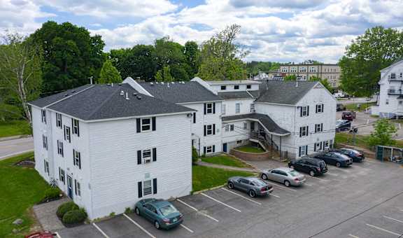 an aerial view of a large white apartment complex with a parking lot and trees in the background