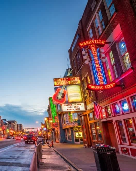 A street view of a city with a brightly lit building that says "Mashville".