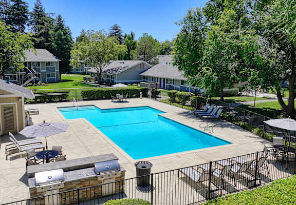a swimming pool with lounge chairs and umbrellas in front of a house at Pinecrest Apartments, Davis ,95616