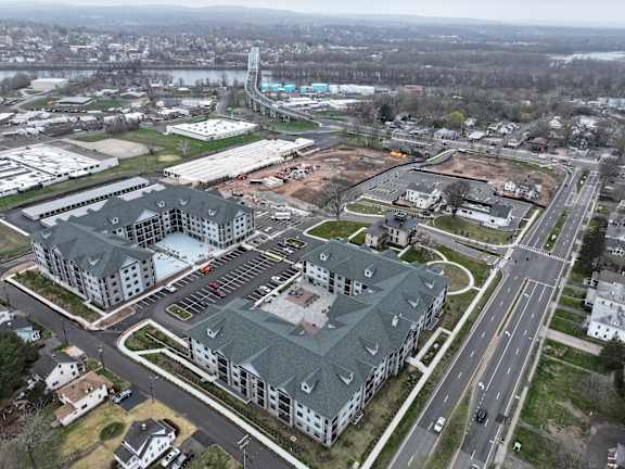 A large, modern building with a green roof is surrounded by a parking lot and other buildings.