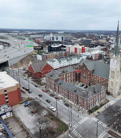 A church with a tall steeple is in the middle of a city intersection.