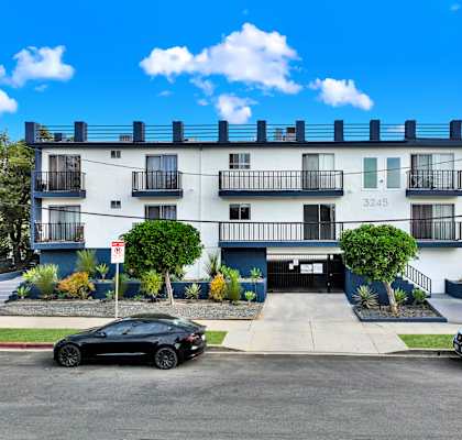 A black car is parked in front of a white building with the number 3245 on it.