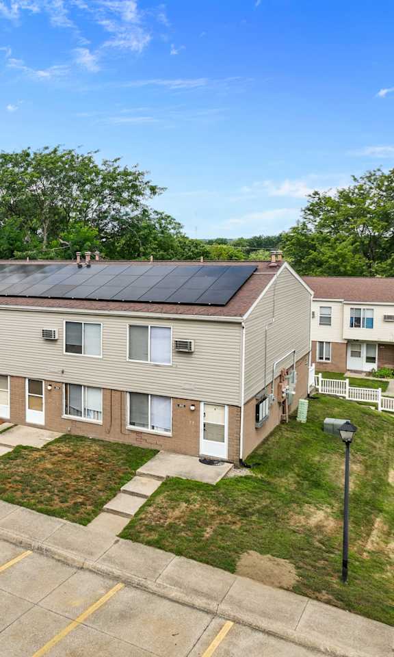 A black car is parked in a parking lot in front of a building with solar panels on the roof.