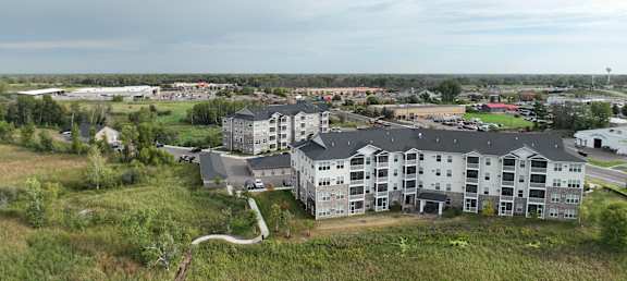 A large white building with a grey roof is surrounded by a grassy field.
