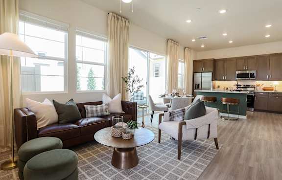 A well-lit living room with a brown leather couch, a green armchair, and a coffee table with a vase of flowers on it.