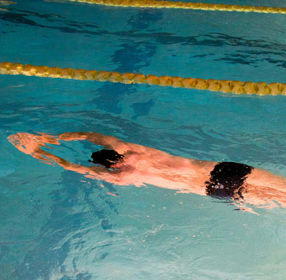 A man swimming in a pool with a yellow lane rope.