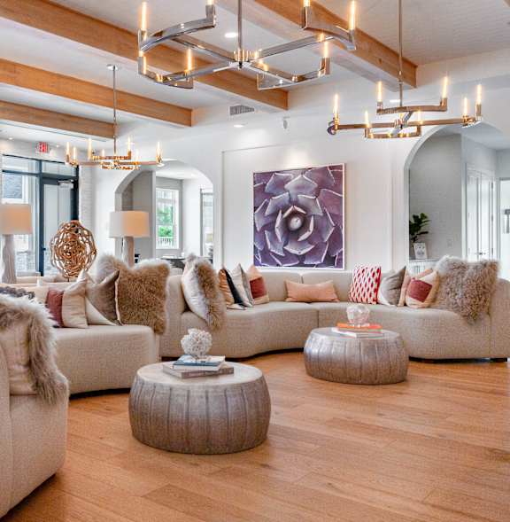 A dog is sitting on a white stool in a living room with a white couch and a wooden coffee table.
