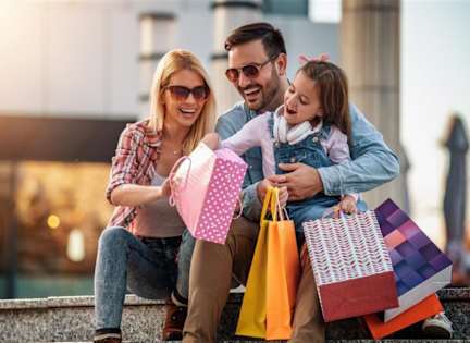 A family of three is sitting together with shopping bags.
