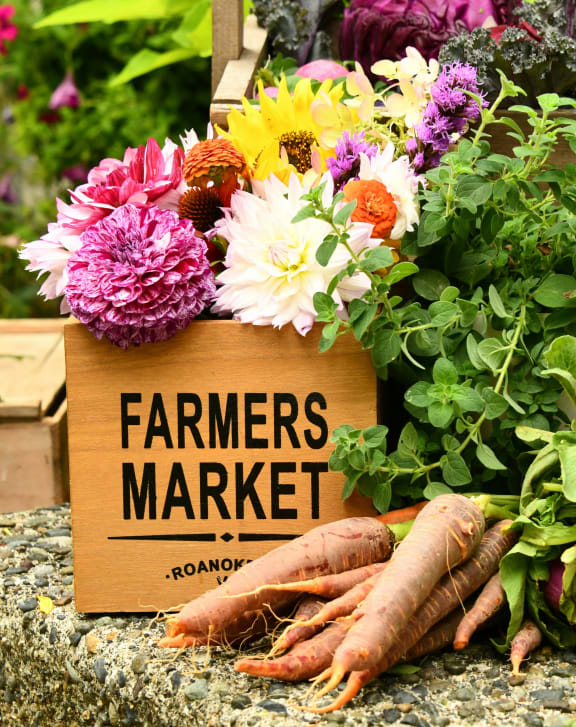 a farmers market with carrots and flowers in a wooden box