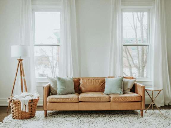 A living room with a tan couch, a white rug, and a white floor lamp.