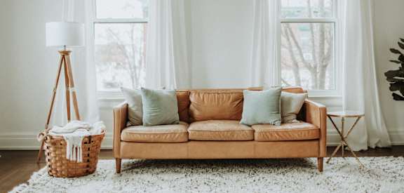 A living room with a tan couch, a white rug, and a white floor lamp.